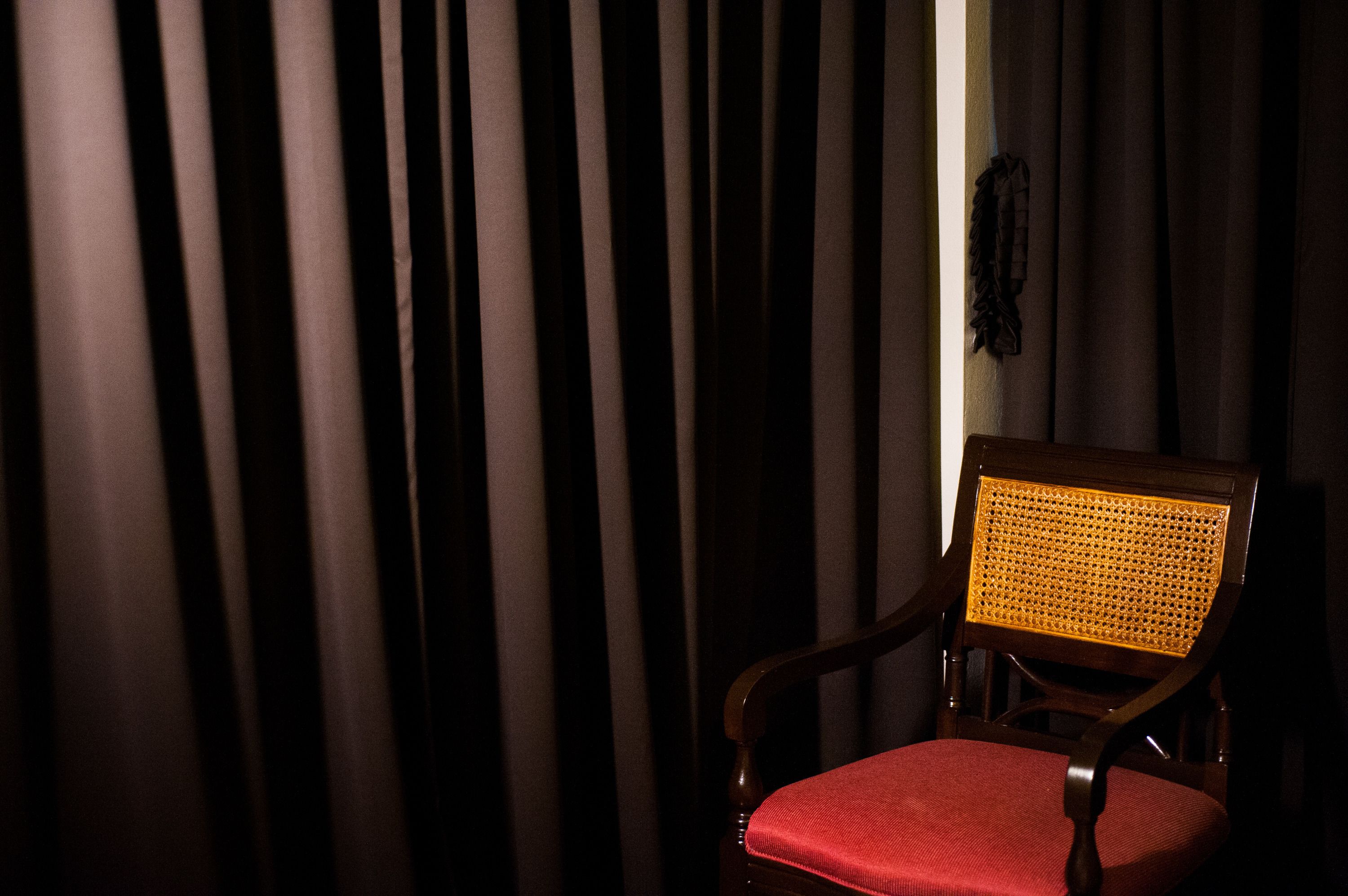 Une chaise dotée d’un dossier en osier et d’un coussin rouge, placée devant un rideau à rayures verticales.