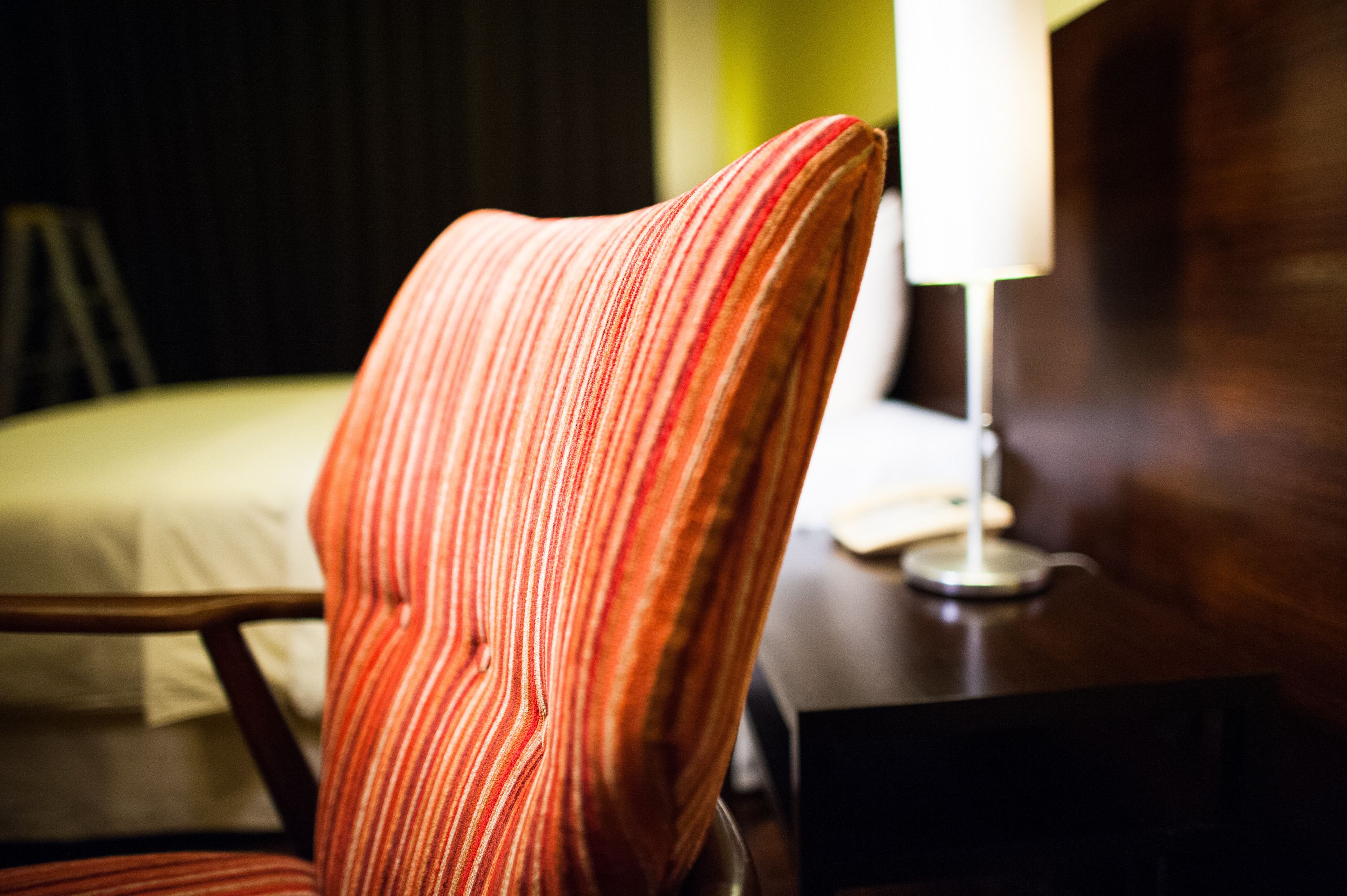Une chambre d’hôtel avec un fauteuil à rayures, une table de chevet avec une lampe et un lit recouvert d’une couverture blanche.