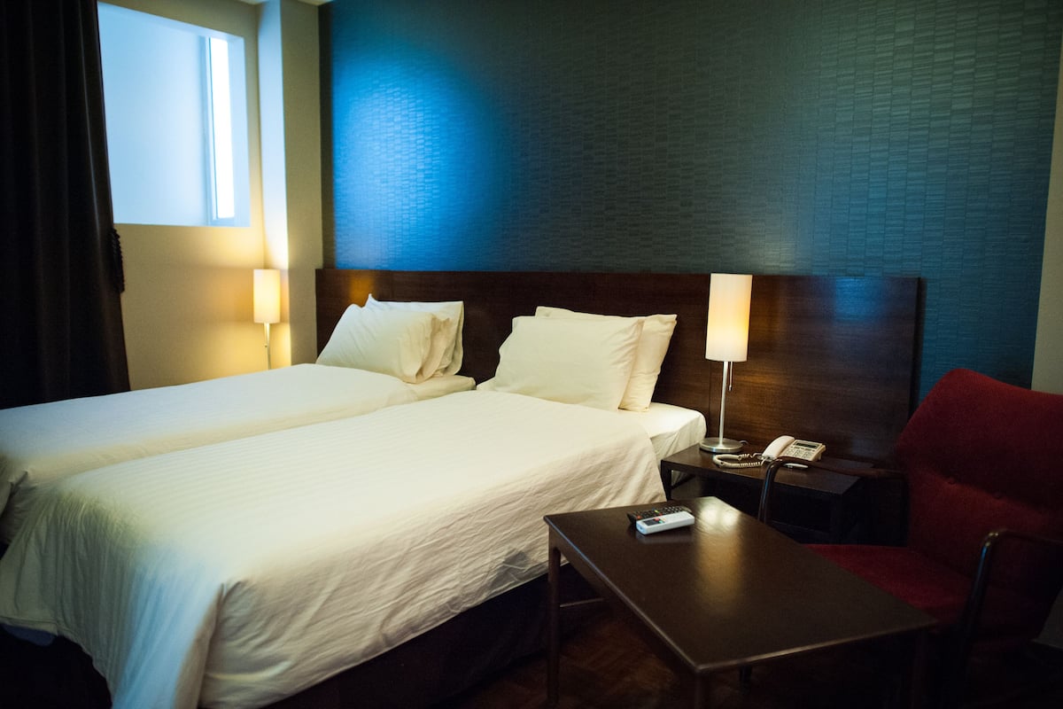 Una habitación de hotel con dos camas, una mesita de noche con lámpara, un teléfono y una silla roja.