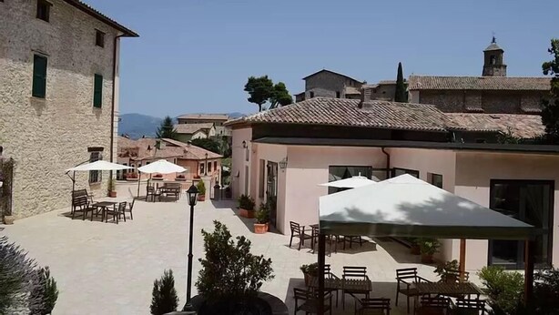 A courtyard with outdoor seating, stone buildings, and a clear sky. - Hotel Della Fonte (Greccio)