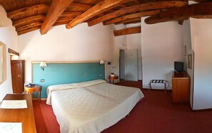 Un dormitorio con una cama grande, un escritorio, una silla, un televisor y una puerta que da a otra habitación.