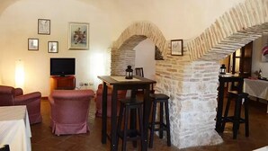 A cozy living room with a stone archway, a dining area with a table and chairs, and a television on a stand. - Hotel Della Fonte (Greccio)