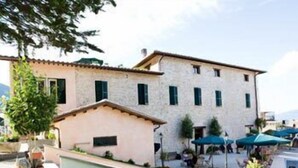 A building with a small attached structure, outdoor seating area with umbrellas, and a well-maintained garden. - Hotel Della Fonte (Greccio)