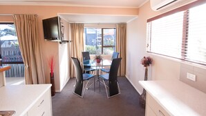 A room with a dining table, chairs, a TV mounted on the wall, and an air conditioning unit. - Anndion Lodge Motel and Function Centre (Whanganui)