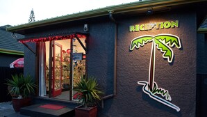 A reception area with a palm tree sign, steps leading up to the entrance, and potted plants. - Anndion Lodge Motel and Function Centre (Whanganui)