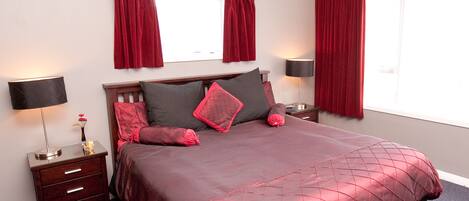 A neatly made bed with a red bedspread, two bedside tables with lamps, a dresser, and a chandelier.