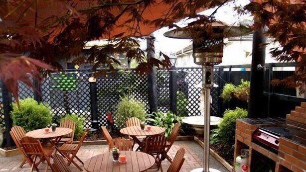 An outdoor patio with round wooden tables and chairs, surrounded by a black lattice fence. - Anndion Lodge Motel and Function Centre (Whanganui)
