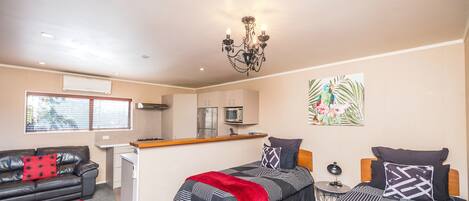 A compact hotel room with two beds, a kitchenette, a sofa, and a dining area.