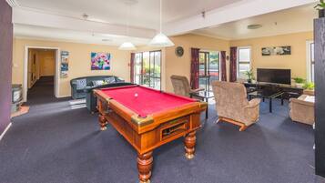A pool table in a room with a sofa, chairs, a television, and a clock on the wall.