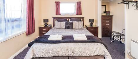 Un lit bien fait, avec une couvre-lit à motifs et des oreillers, une fenêtre avec des rideaux, une commode avec des tiroirs et une chaise.