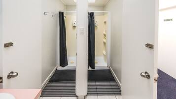 A narrow, enclosed shower area with black curtains, a white door, and a tiled floor.