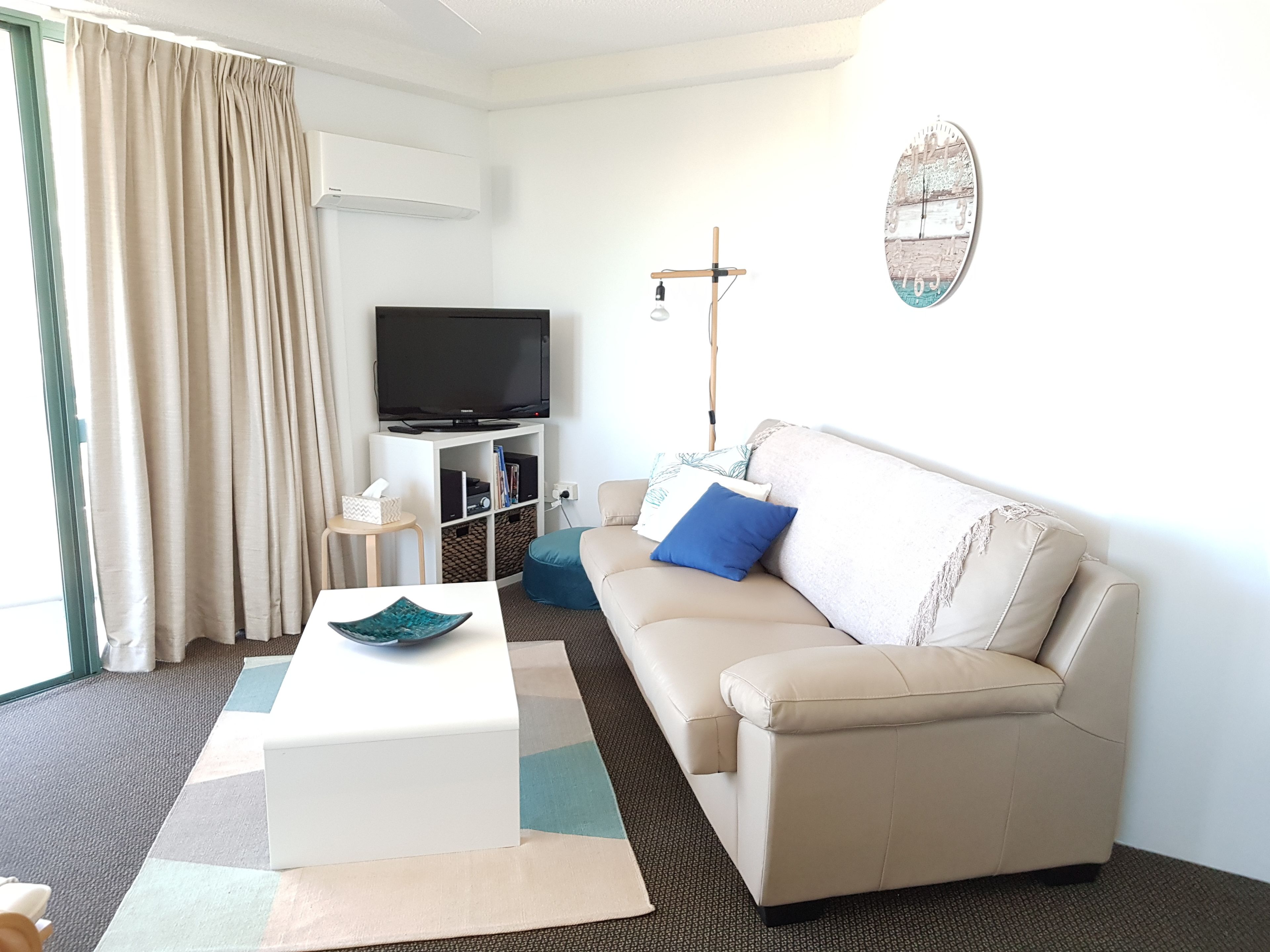A living room with a sofa, a coffee table, a TV, and a wall-mounted light fixture.