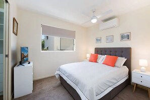 A bedroom with a bed, nightstands, a TV, a ceiling fan, and a window. - Excellsior (Mooloolaba)