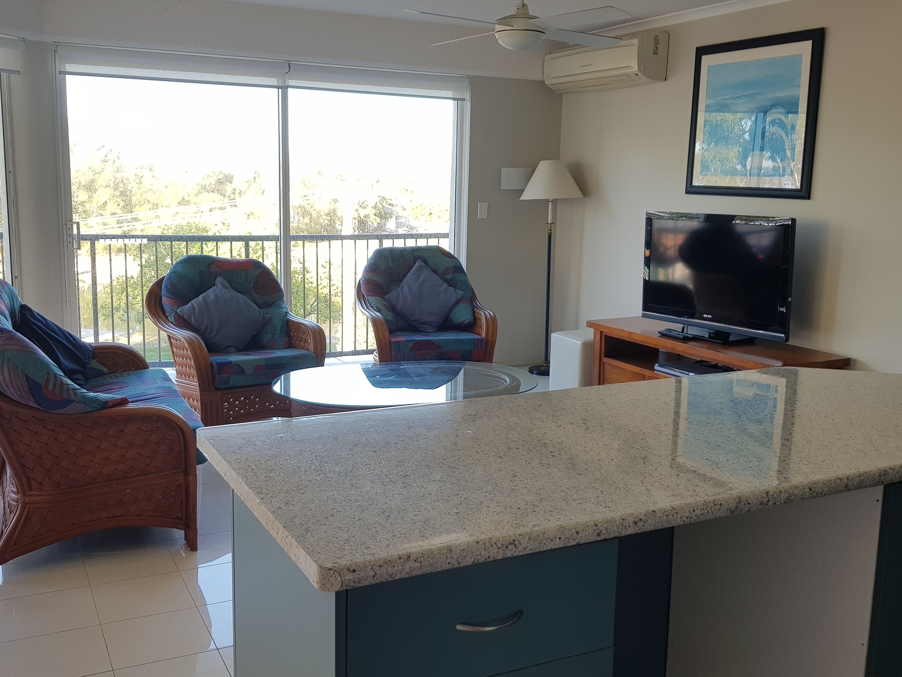 A living room with a TV, two armchairs, a coffee table, and a balcony with a view.