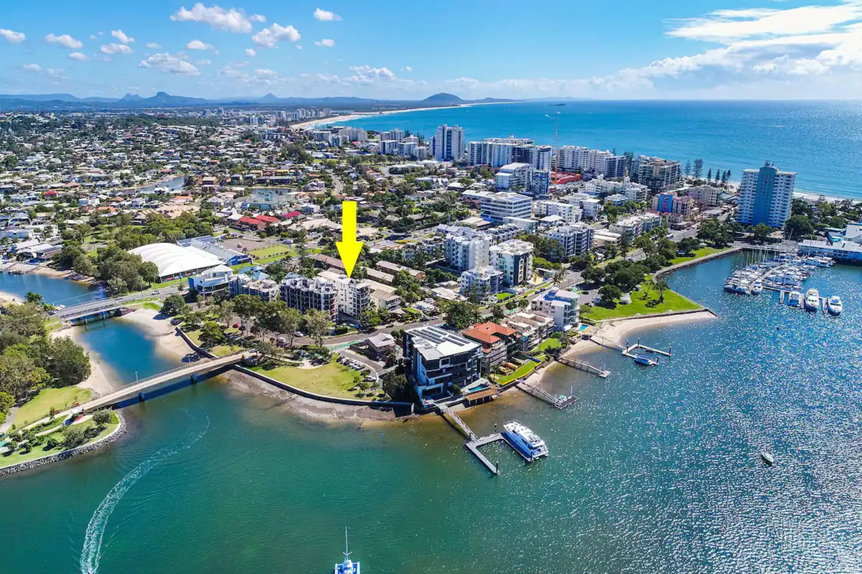 Vue aérienne d’une ville côtière avec un port de plaisance, des immeubles résidentiels et un pont reliant deux quartiers.