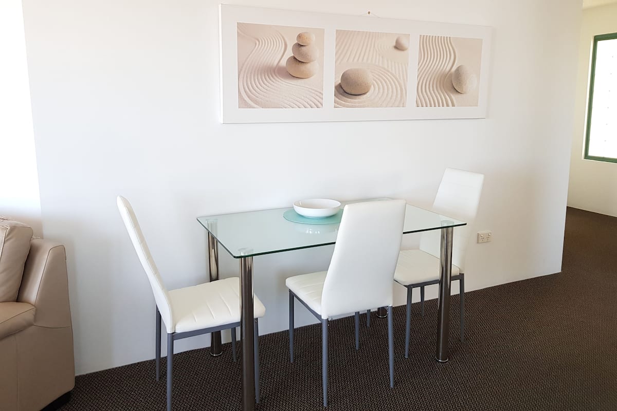 A modern room with a glass table, white chairs, and a framed abstract artwork on the wall.