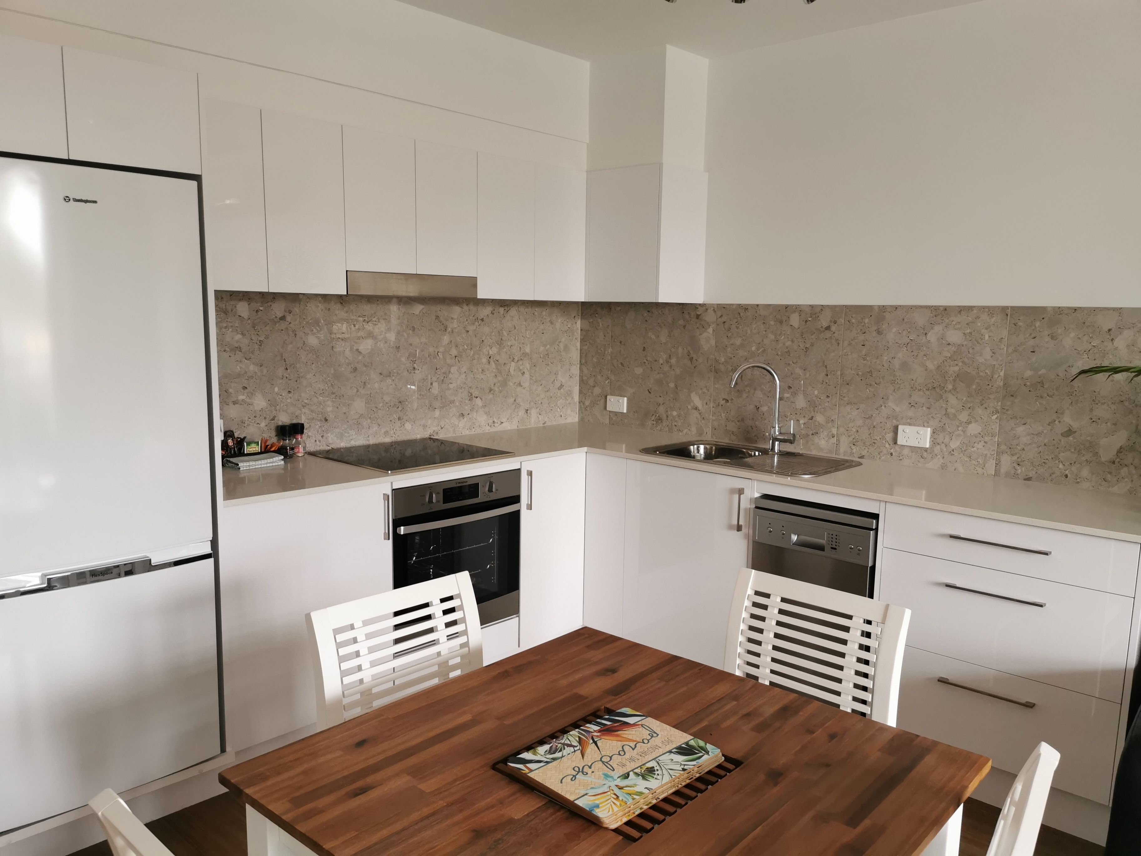 Een moderne keuken met witte kastjes, een houten eettafel en een spatwand van gevlekte tegels.