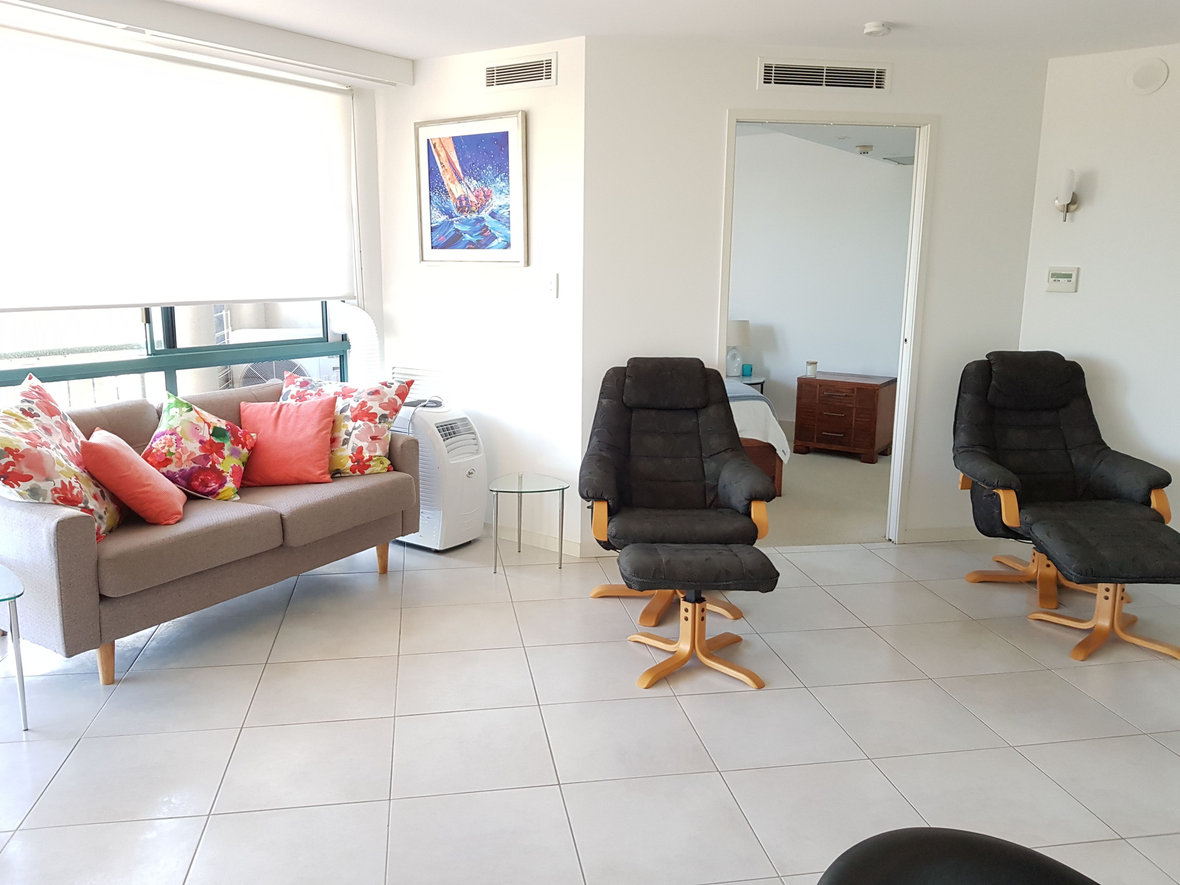 Un salon avec un canapé, deux fauteuils noirs, une petite table et une grande fenêtre.