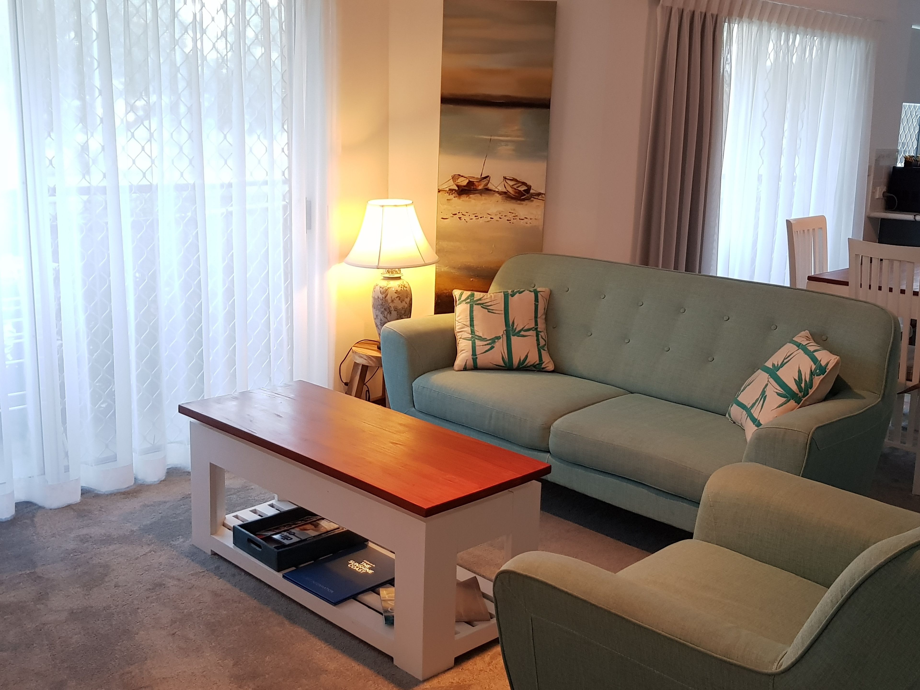 A living room with a sofa, a coffee table, and a lamp. There is a bookshelf with books and a decorative item.