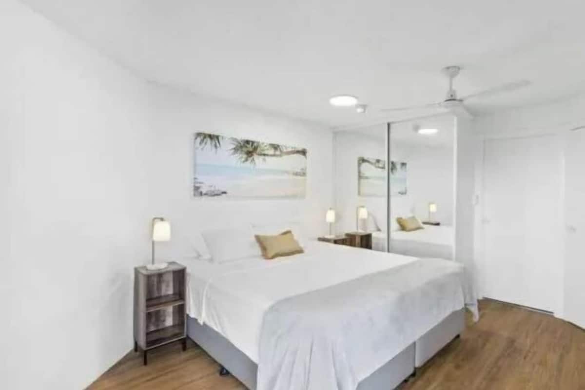 A bedroom with a bed, bedside tables, a ceiling fan, a large mirror, and a wall-mounted picture.