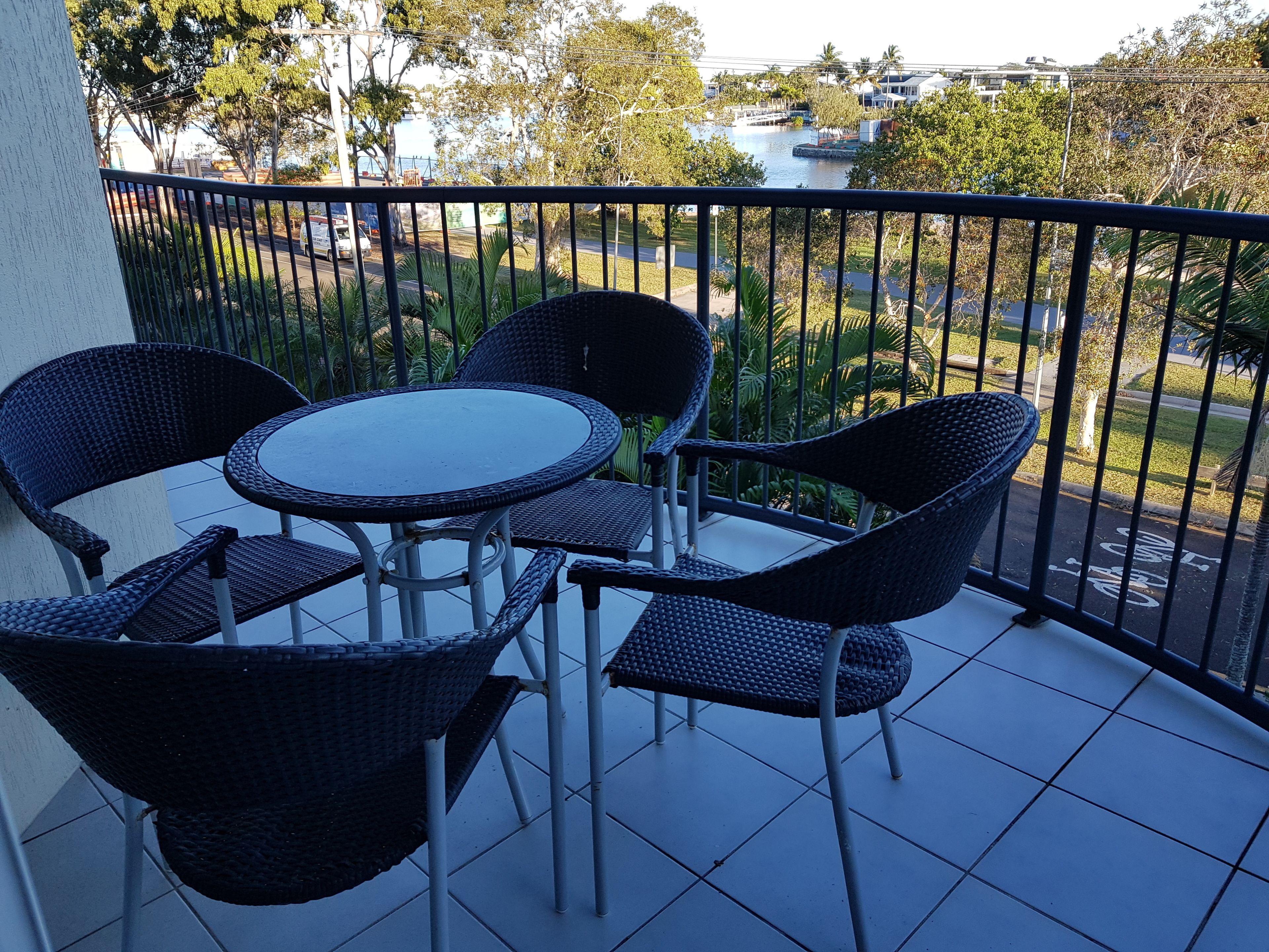 Un balcon avec une table ronde et quatre chaises, donnant sur une rivière et une végétation luxuriante.