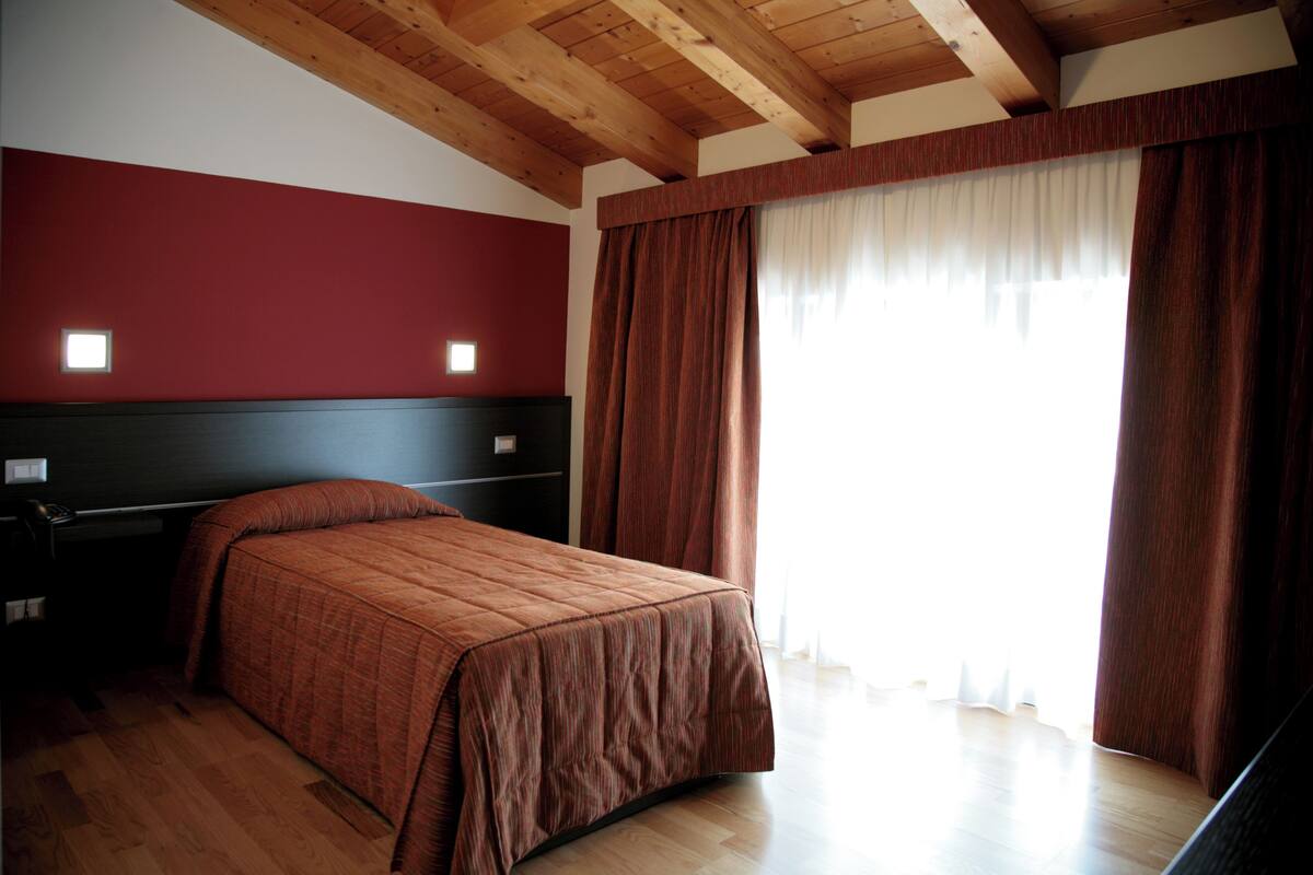 A bedroom with a wooden ceiling, a bed with a brown bedspread, a nightstand, and a window with curtains.