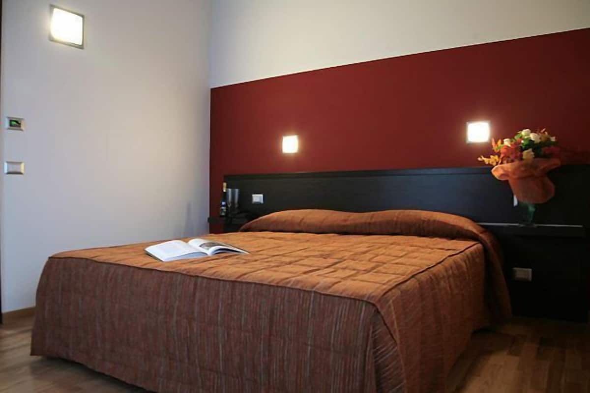 A bedroom with a bed, a nightstand, a vase with flowers, and two wall-mounted lights.