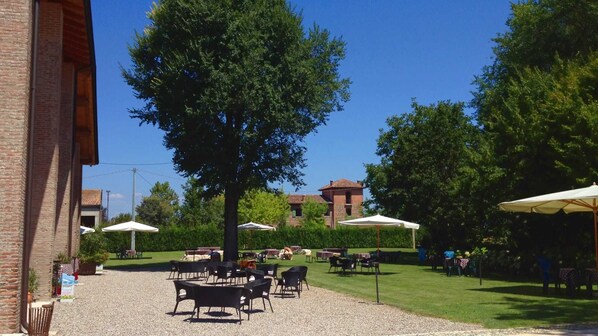 An outdoor seating area with tables and chairs, surrounded by trees and a building in the background.