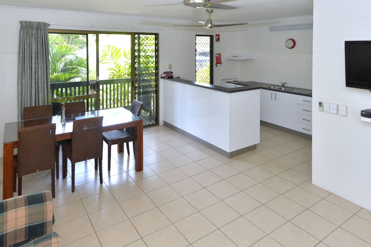 Una cocina moderna con armarios blancos, una isla integrada y un comedor con sillas de mimbre y una mesa de vidrio.