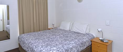 A bedroom with a bed, a wooden nightstand, a mirror, and a window with curtains.