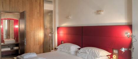 A hotel room with a large bed, a wooden wardrobe, a vanity with a mirror, and a red headboard.