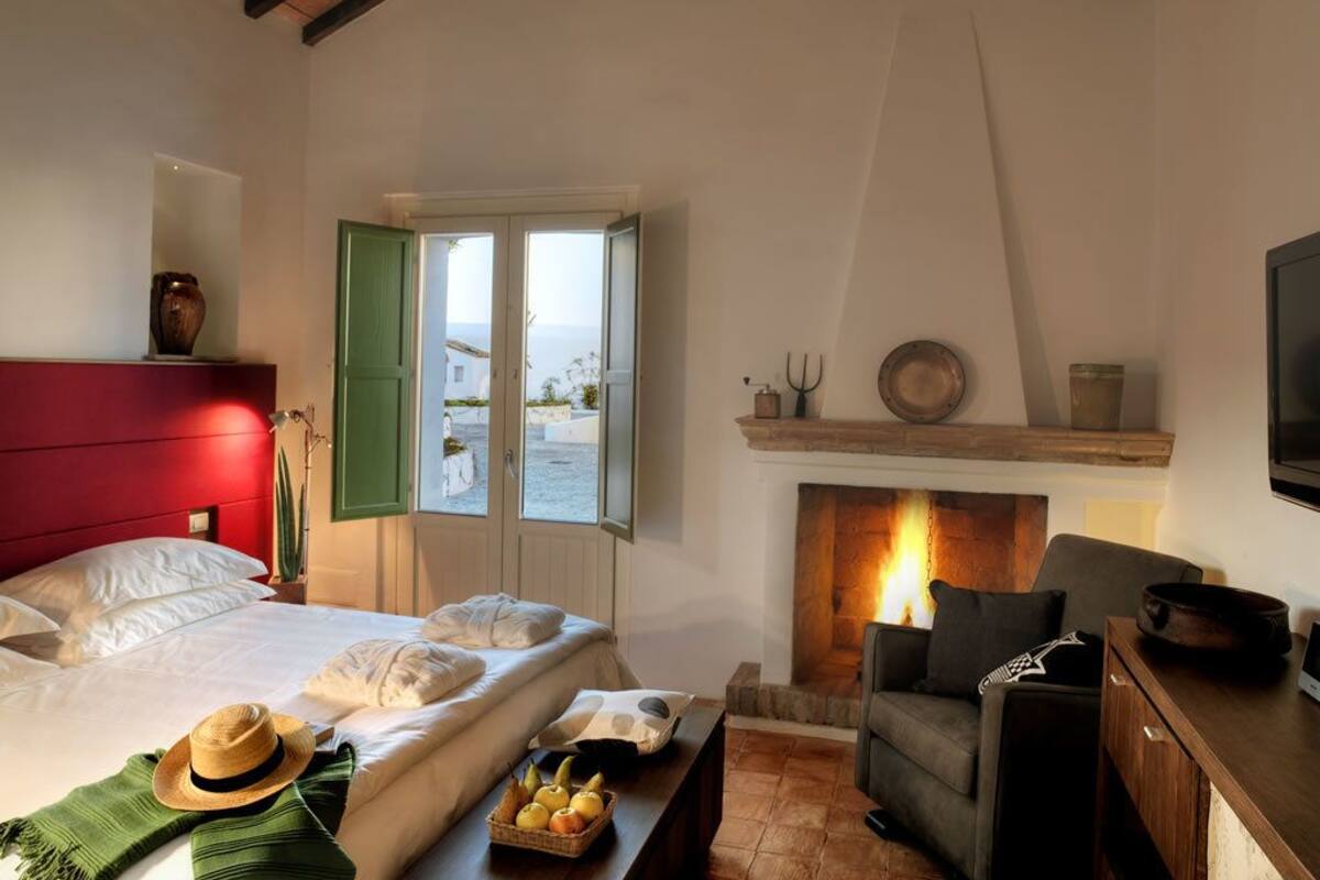 Un dormitorio con cama, chimenea, sofá y vistas al exterior.