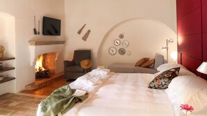 A cozy bedroom with a fireplace, a bed with pillows, a chair, and a wall with decorative plates. - Torre Fiore Hotel Masseria (Pisticci)