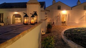A courtyard with a paved walkway, a potted plant, and a well-lit entrance with a door and windows. - Torre Fiore Hotel Masseria (Pisticci)