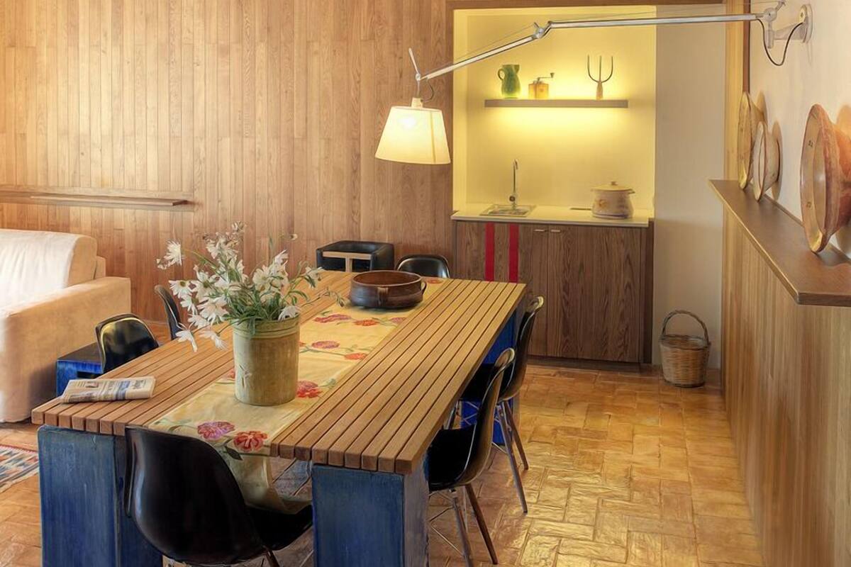 Una habitación acogedora con una mesa de comedor de madera, sillas, un sofá y una cocina con una lámpara moderna.