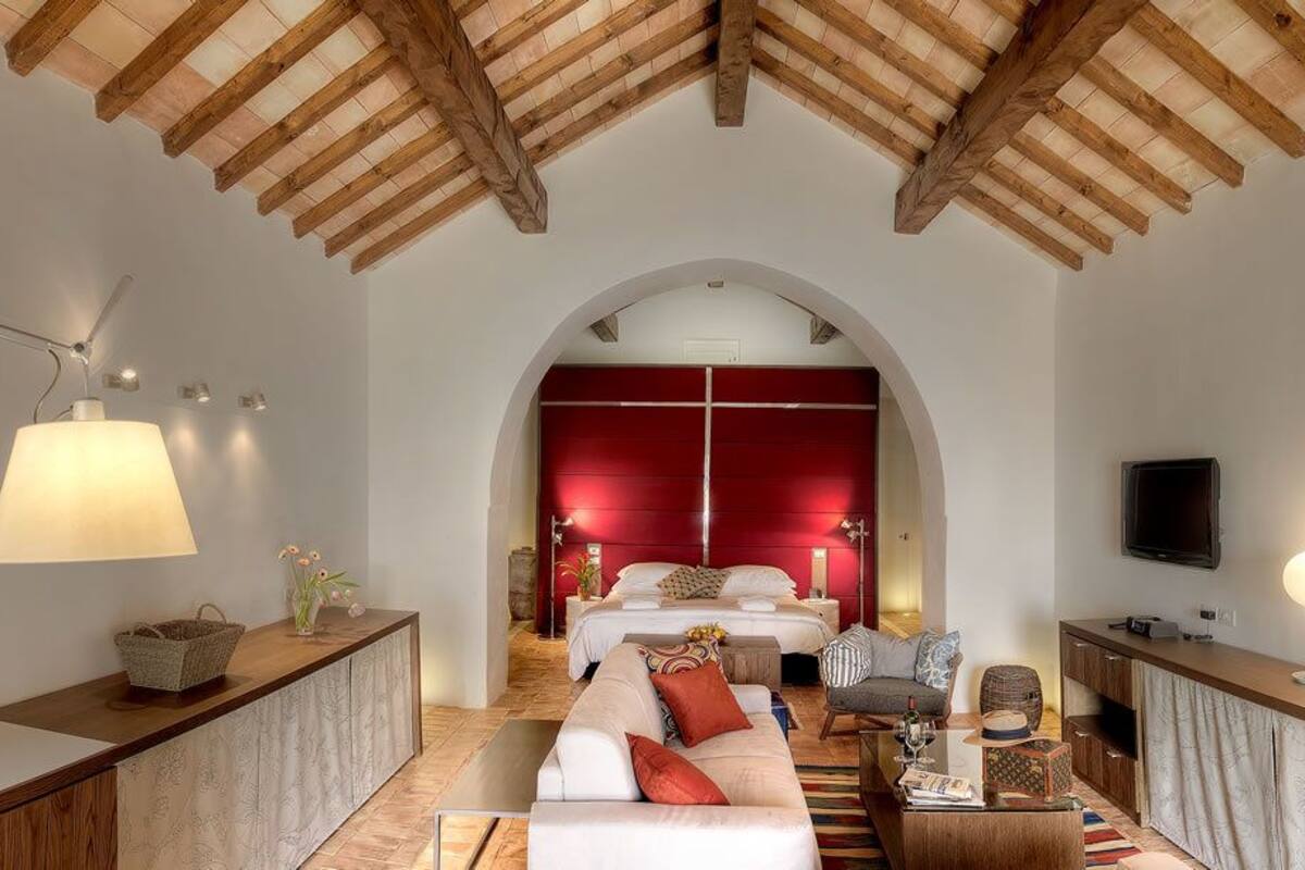 Un dormitorio con cabecera roja, una cama, una mesita de noche, una lámpara y un televisor.