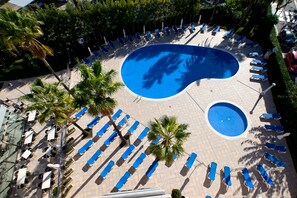 Zona de piscina con múltiples sillas de descanso y palmeras.