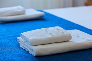 Una toalla blanca doblada con cuidado, con texto en relieve sobre otra toalla azul, sobre una cama.