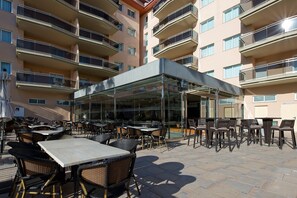 Un patio al aire libre con mesas y sillas, un área de estar cubierta y un edificio con varios balcones.