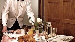A person in a white uniform with gold epaulettes serving breakfast on a table with croissants, a bottle of orange juice, and a vase with a white flower. - Villa Venezia (Odesa)