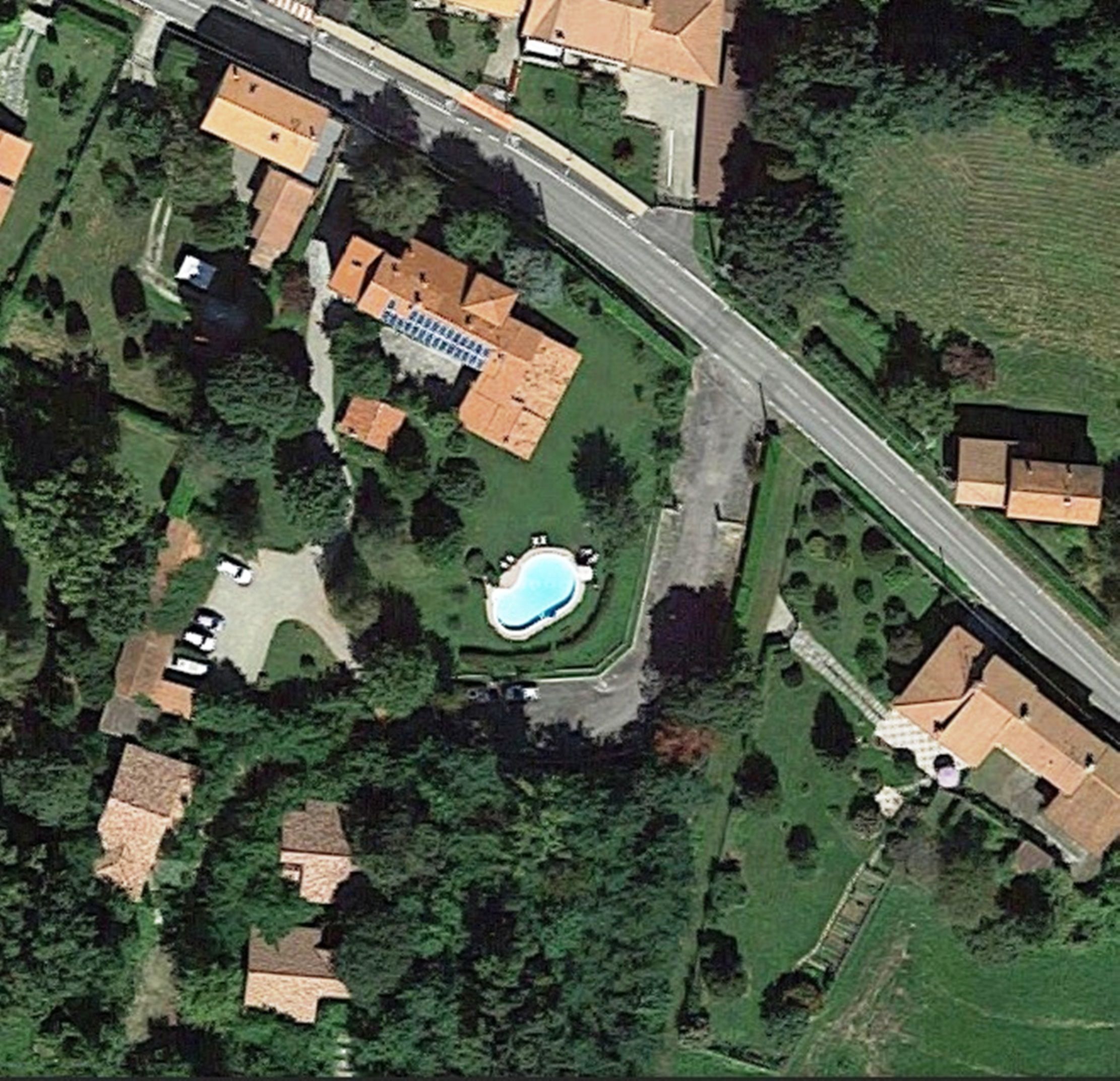 An aerial view of a residential area with houses, a swimming pool, and a road.