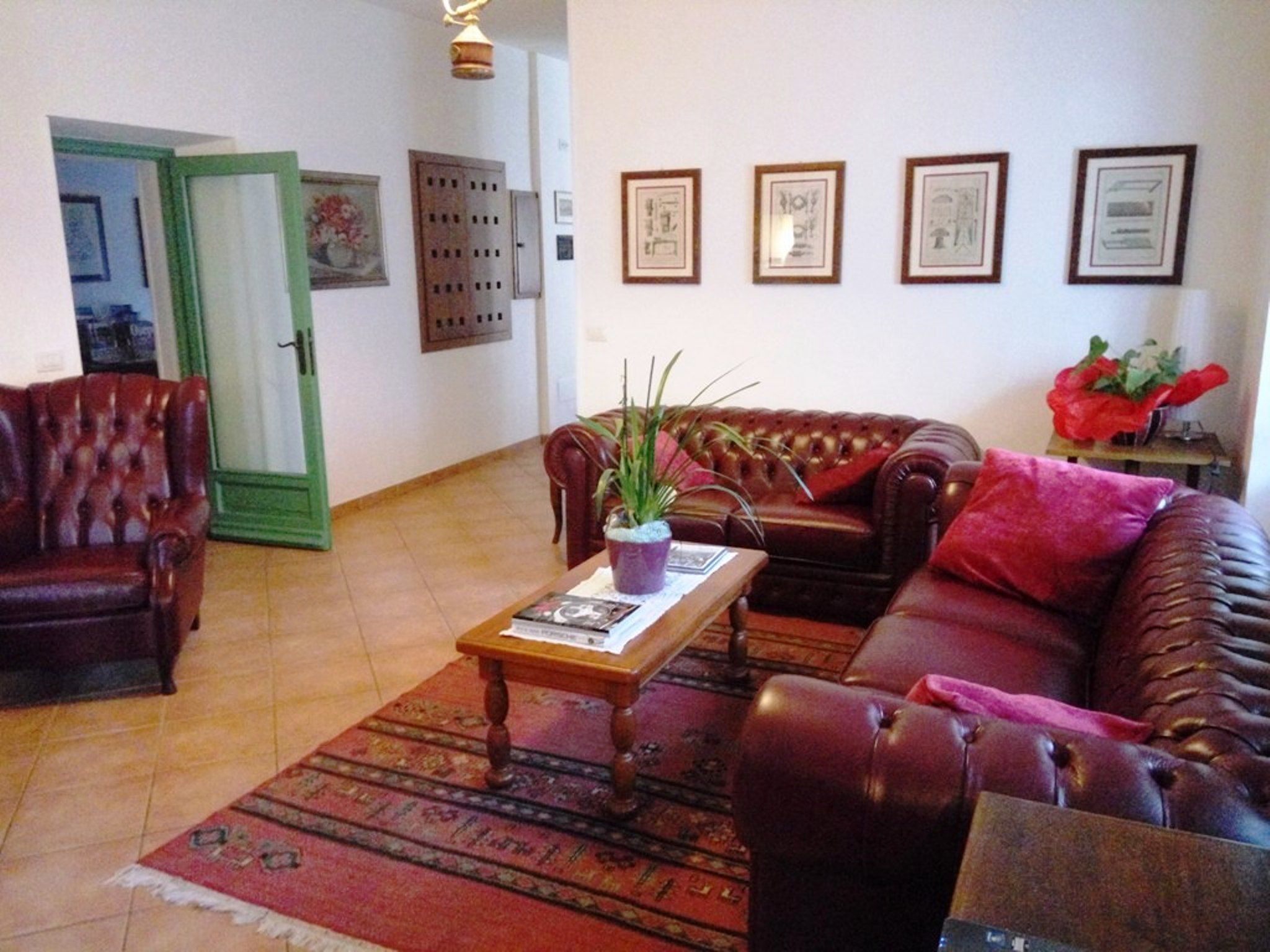 A living room with a brown leather sofa, a matching armchair, a wooden coffee table, and a patterned rug. There are framed pictures on the wall and a green door in the background.