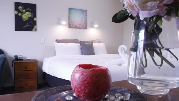 Quarto de hotel com cama, mesa de cabeceira e um vaso com flores.