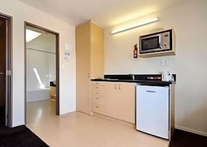 Una cocina compacta con microondas, un refrigerador pequeño y un lavamanos.