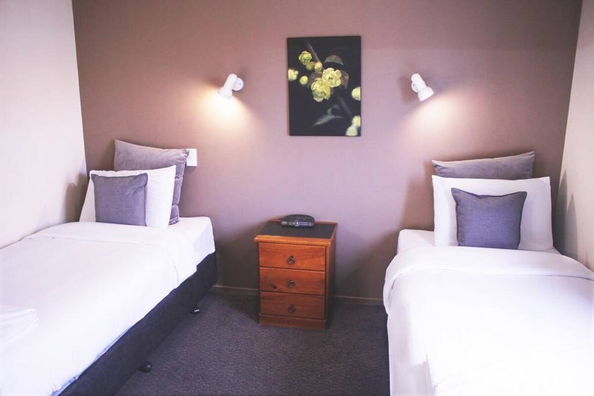 Une chambre d’hôtel avec deux lits simples, une petite table de chevet en bois et un tableau accroché au mur.