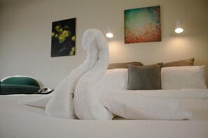 A neatly made bed with a white towel arranged in a decorative shape, a green chair, and two paintings on the wall. - Papanui Court Motel (Christchurch)
