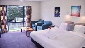 Quarto de hotel com uma cama grande, duas poltronas, uma mesa pequena e uma varanda com cortinas.