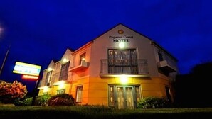 Um motel com uma placa indicando 'Pagani Court Motel' sob um céu crepuscular.