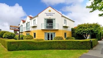A two-story Paparati Court Motel with a balcony on the second floor, a well-maintained lawn, and a clear sky.