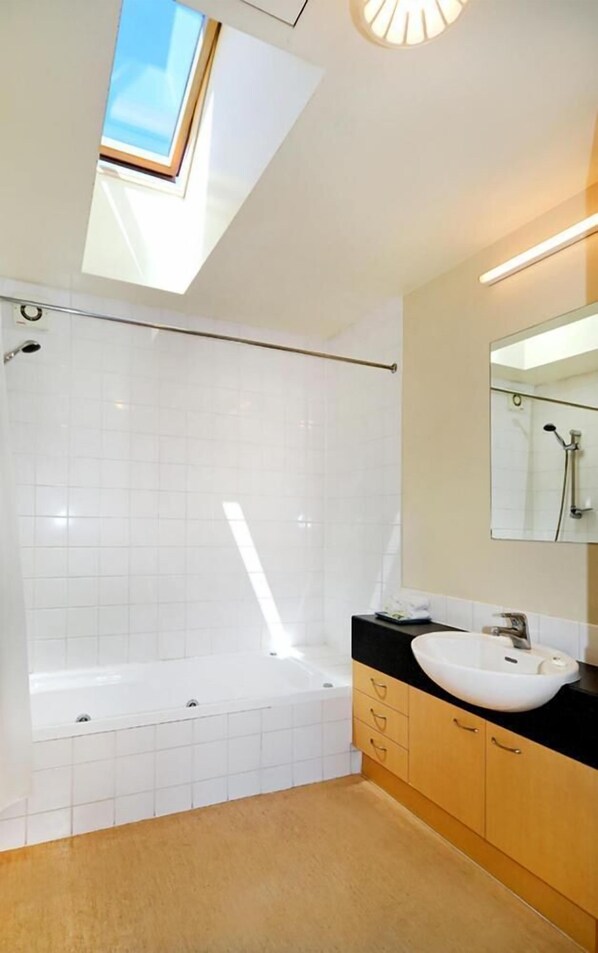 Un baño moderno con tragaluz, bañera, lavamanos y armarios de madera.